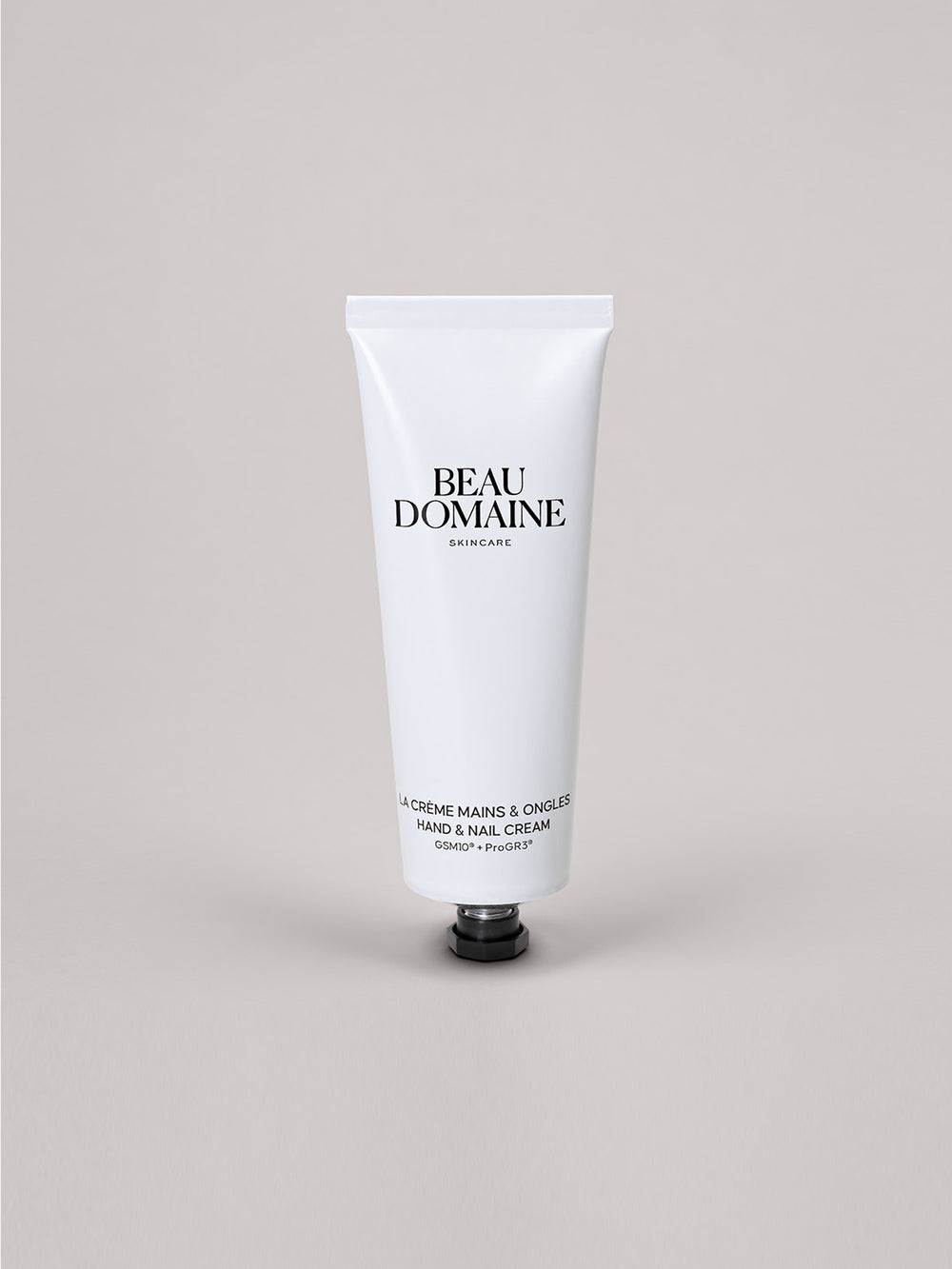 White tube of Beau Domaine hand and nail cream on a light gray background